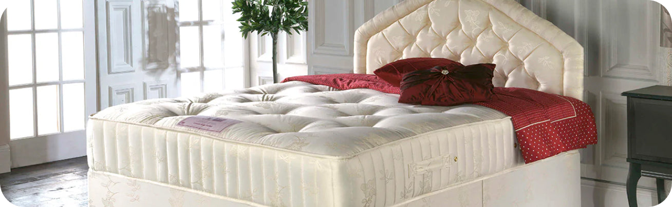 Quilted cream mattress on an upholstered bed frame with decorative pillows and red bedding.