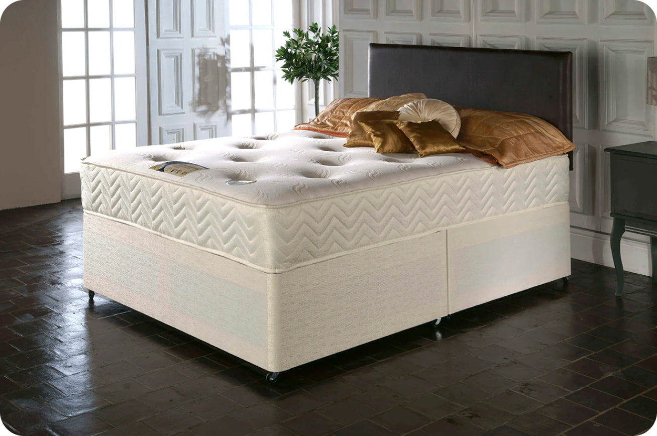 Cream-colored mattress with tufted design on a bed frame, embellished with gold and brown decorative pillows.