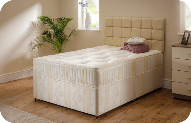 Beige upholstered bed frame with a quilted headboard and a cream mattress, featuring a decorative throw blanket.
